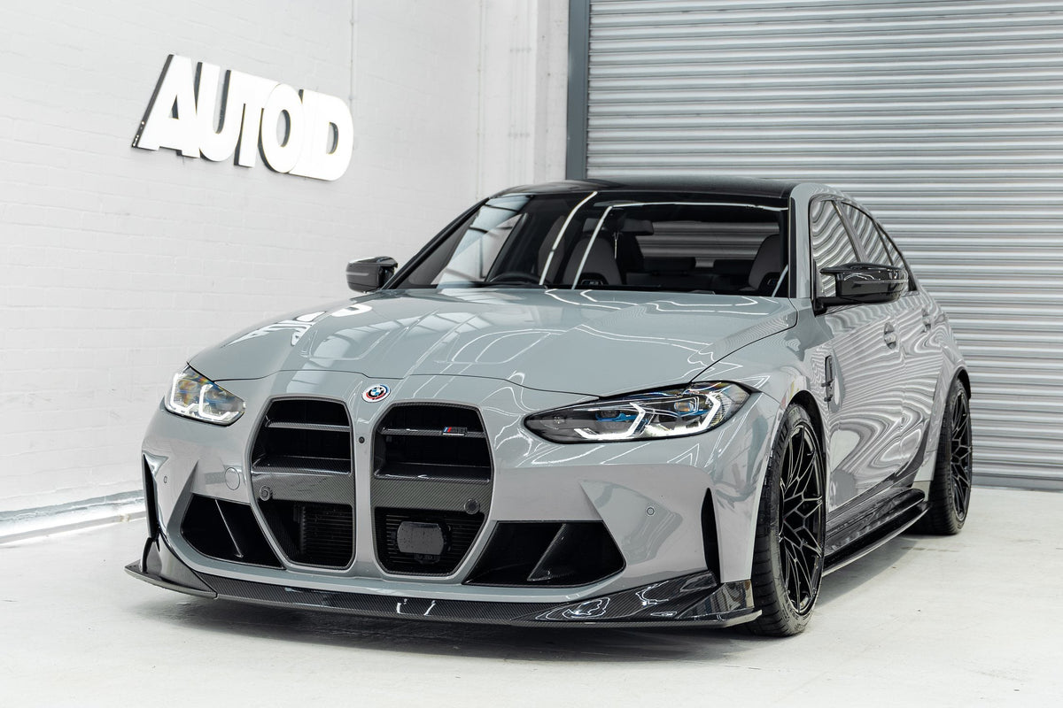 Grey BMW G80 M3 front three-quarter in the AUTOID workshop with TREVORA PR-1 carbon splitter and FORM carbon GT kidney grilles, front plate removed