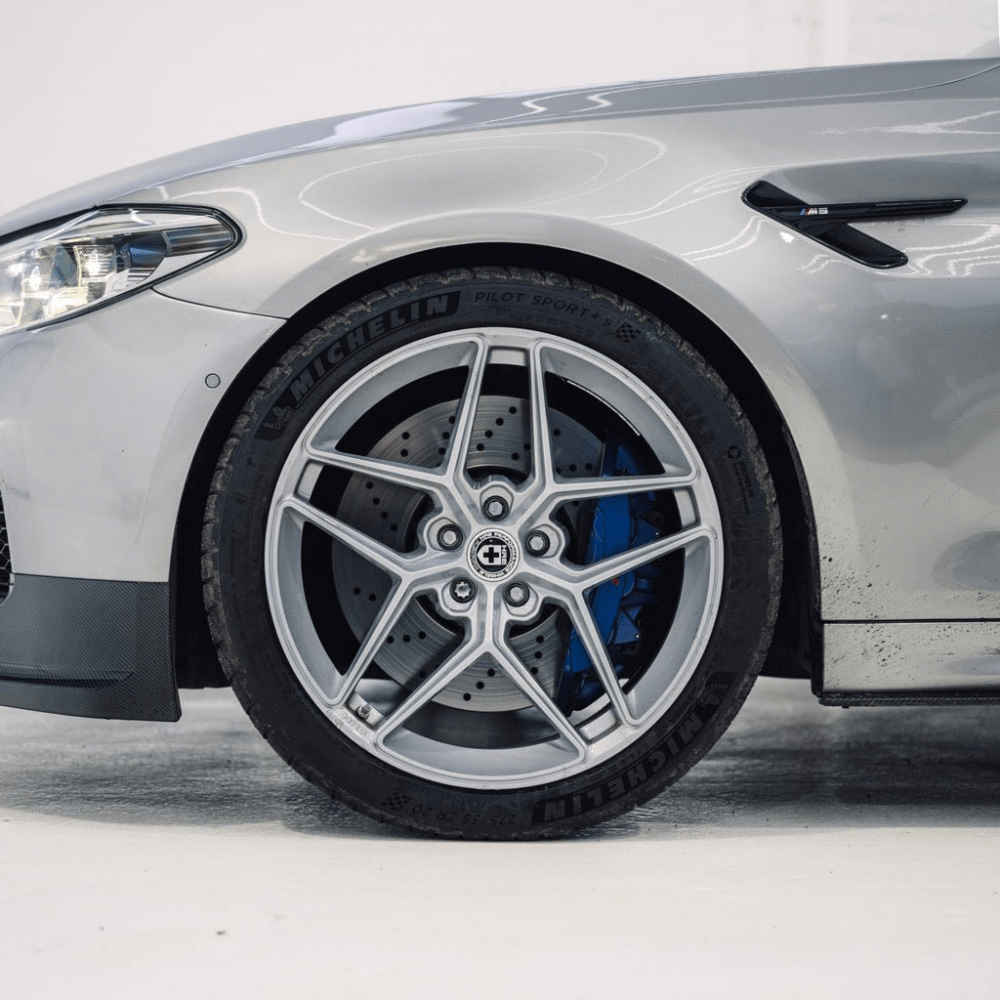 Close-up of a car wheel with a silver rim and blue brake caliper on a white background