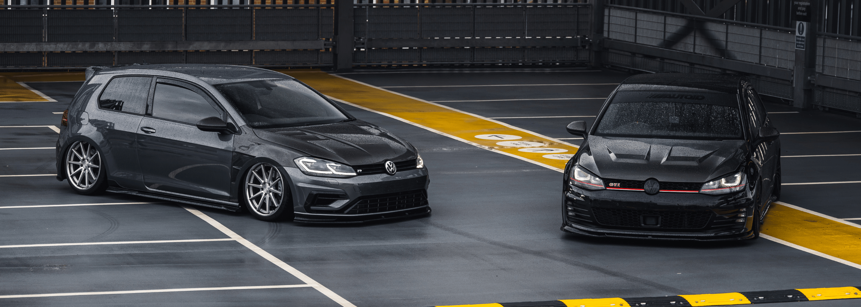 Two black cars parked side by side on a parking lot with a yellow line.
