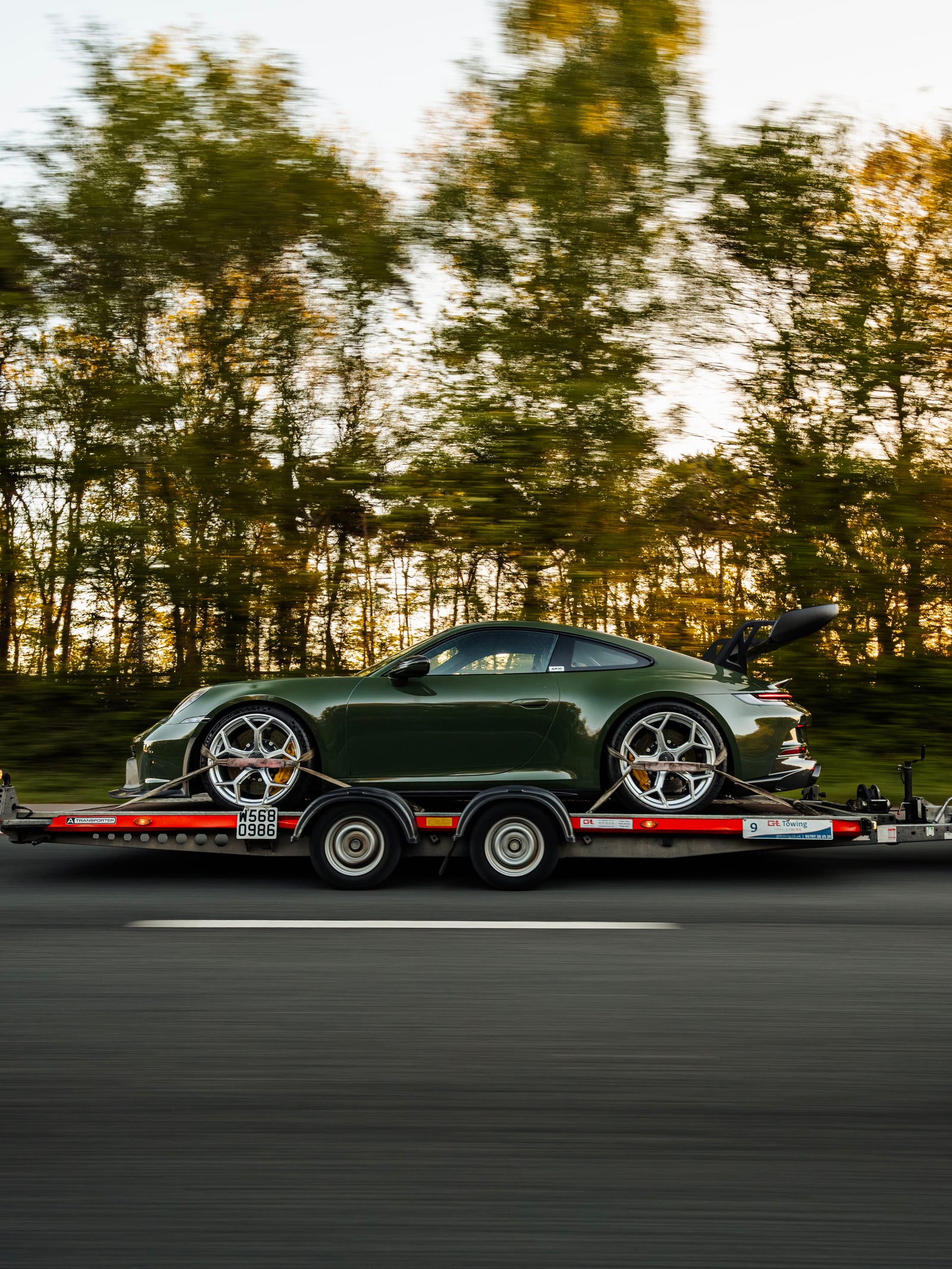Side of modified Porsche 992 GT3 with ADRO body kit on trailer being towed