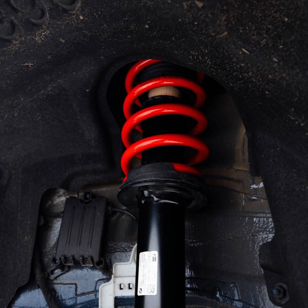 Close-up of a car suspension shock absorber with red coil spring on a dark background