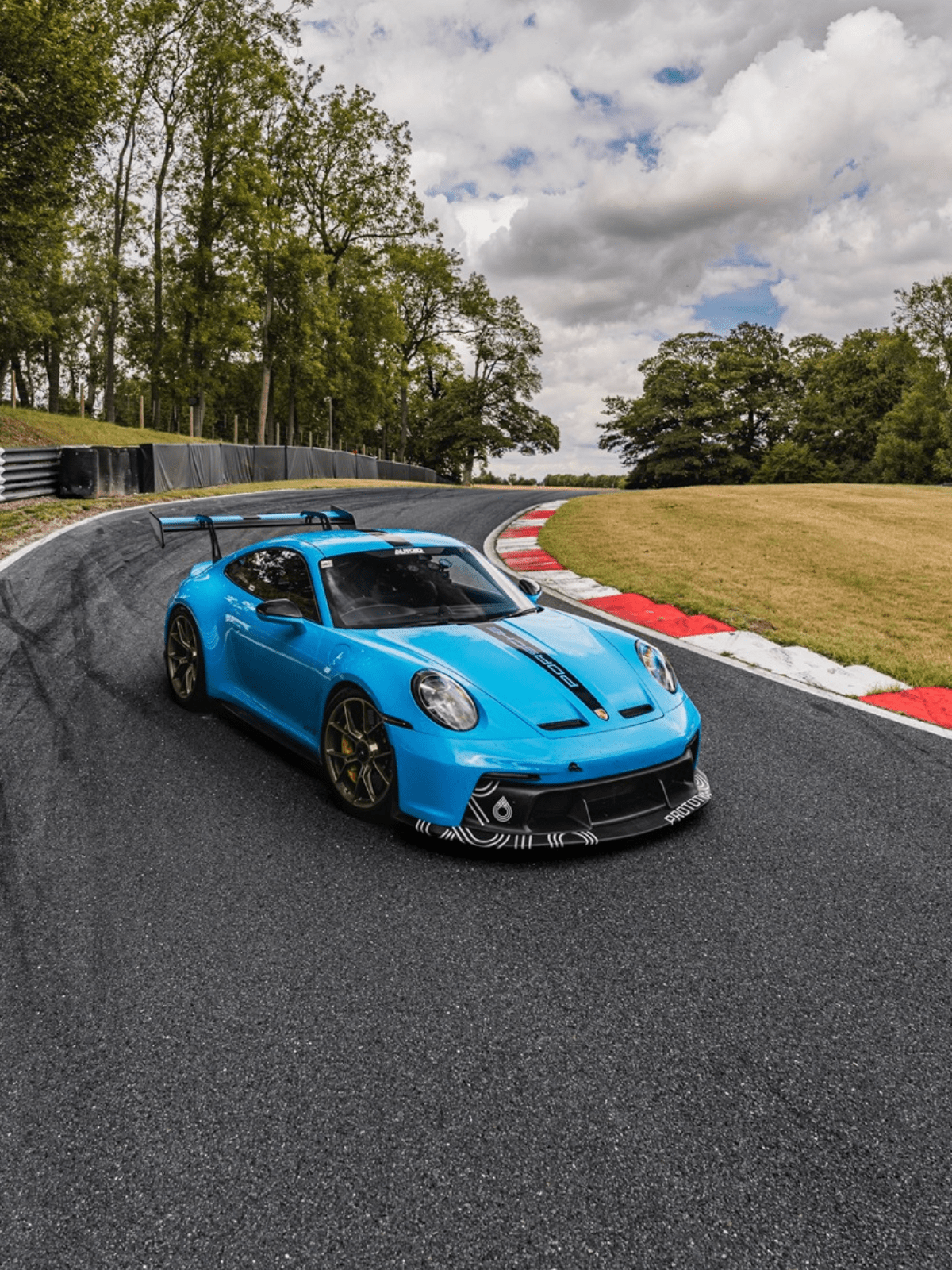Blue sports car on a racetrack with trees and sky in the background