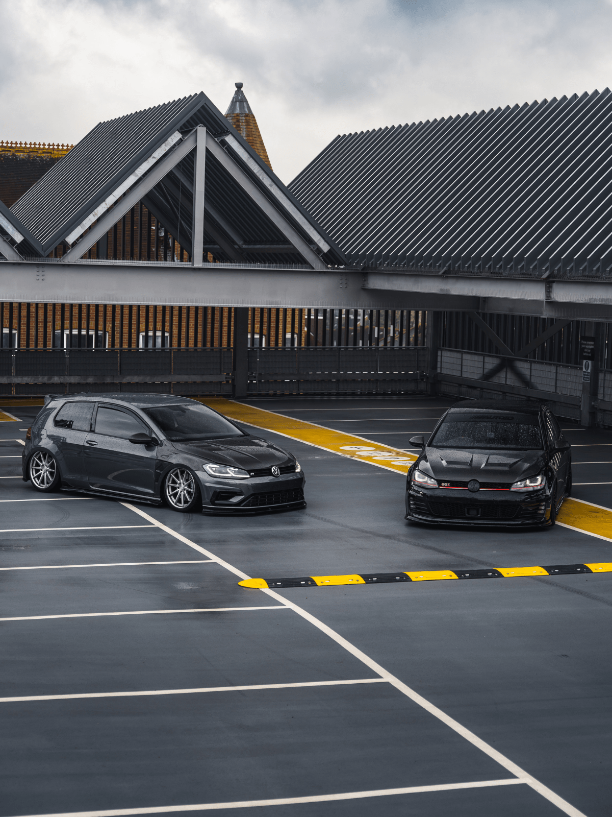 Two black cars parked on a parking lot with a building in the background